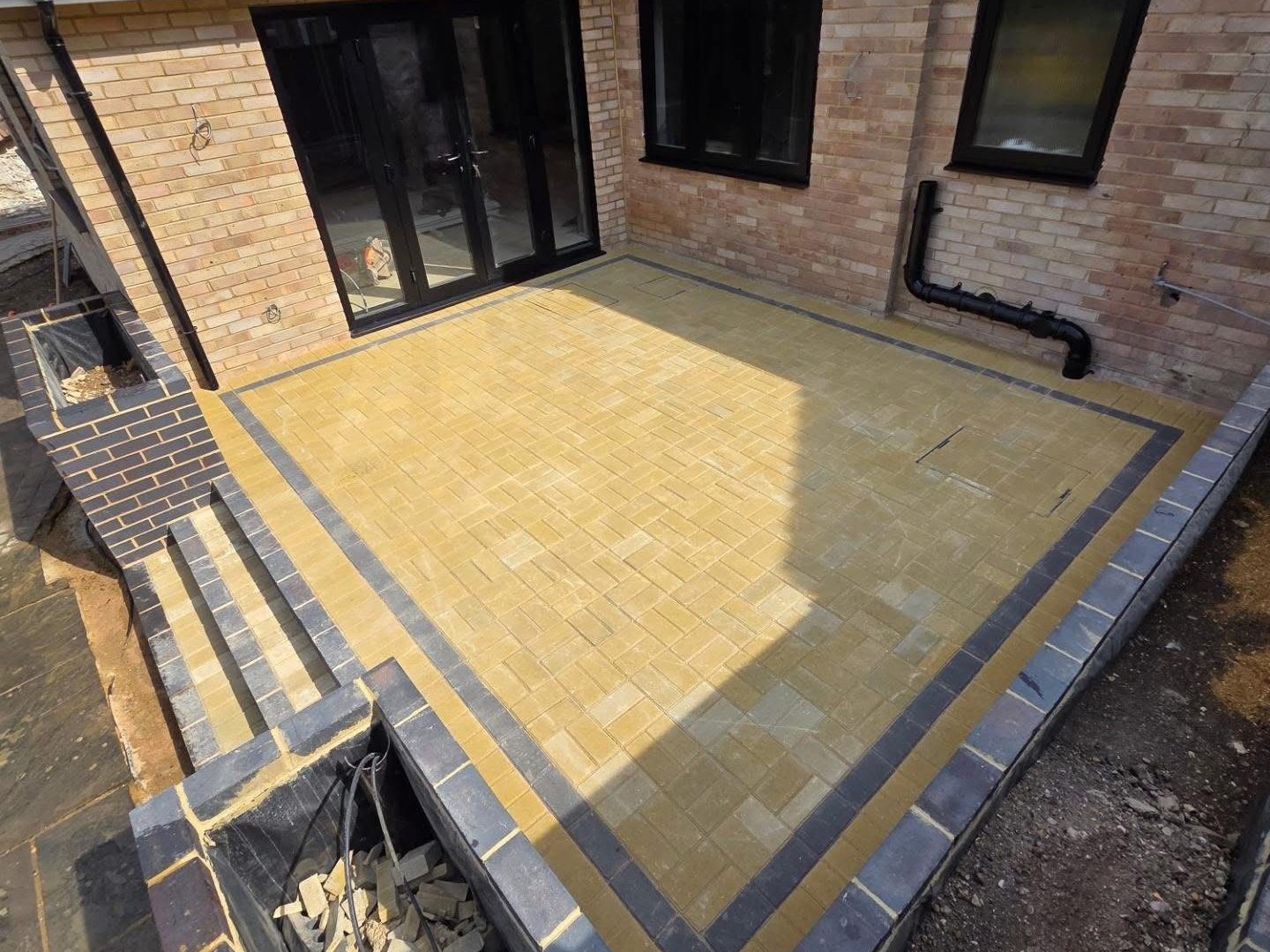 Raised buff block paved patio with a charcoal border outside bifold doors