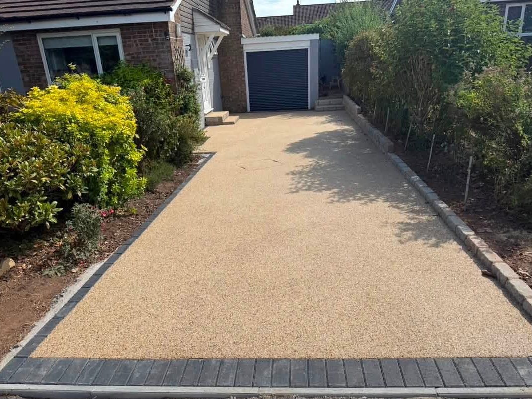 Buff resin bound driveway with charcoal block edging beside a bungalow